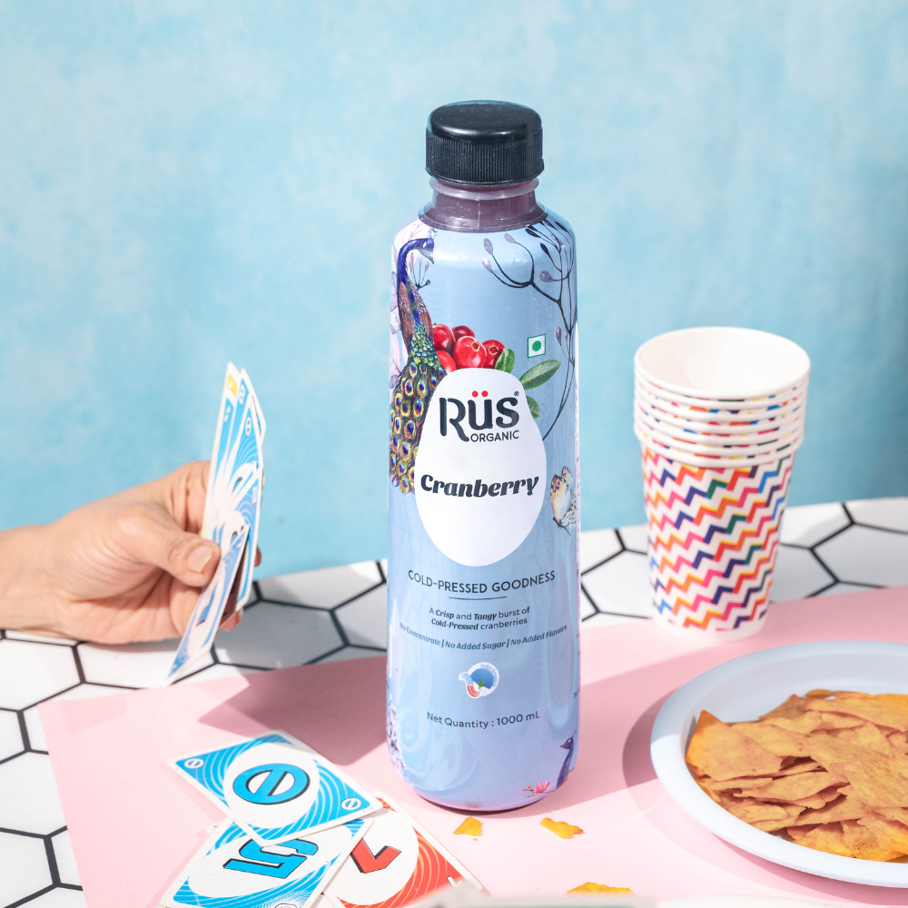 Organic cranberry juice bottel of rus organic in center of the table where some kids are playing uno and having lunch